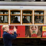 A young person photographs a Coca-Cola branded tram in Lisbon.